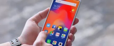 Optimiser son smartphone : image, photo d'une main qui tient un téléphone affichant un écran clair avec le mot “Settings” ou “Réglages” visible.