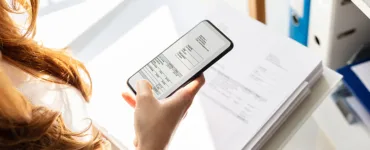 Image, photo d'un smartphone tenu au-dessus d’un document avec la caméra activée, simulant un scan.