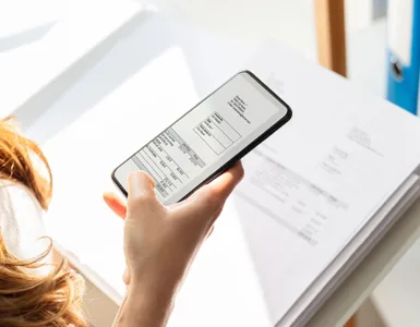 Image, photo d'un smartphone tenu au-dessus d’un document avec la caméra activée, simulant un scan.