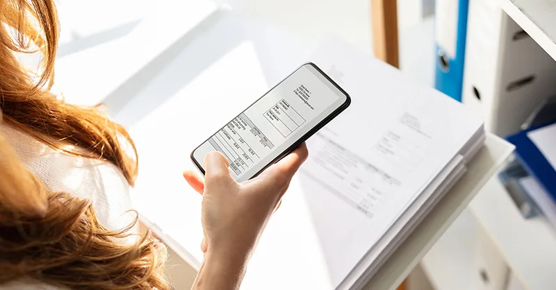 Image, photo d'un smartphone tenu au-dessus d’un document avec la caméra activée, simulant un scan.