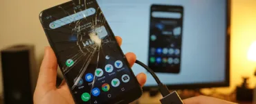 Téléphone avec écran cassé : image ou photo d'un smartphone Android avec un écran fortement fissuré au premier plan. L’écran affiche une interface légèrement visible (comme des icônes ou un écran d’accueil flou). Une main tient une souris branchée au téléphone avec un câble OTG.