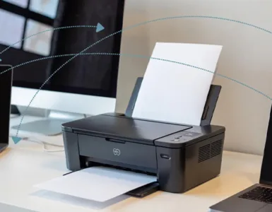 Partage d'une imprimante : image ou photo d'un bureau moderne avec deux ordinateurs portables et un ordinateur de bureau connectés à une même imprimante Wi-Fi au centre. Des lignes de connexion discrètes illustrent le réseau local entre les appareils et l'imprimante.